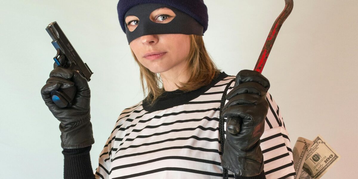 Photo by Vika Glitter: https://www.pexels.com/photo/a-woman-in-striped-shirt-carrying-a-black-bag-while-holding-a-gun-7916847/