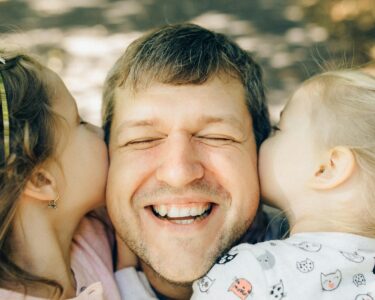 Photo by Nataliya Vaitkevich: https://www.pexels.com/photo/close-up-of-a-man-being-kissed-by-his-daughters-5290404/