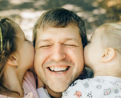 Photo by Nataliya Vaitkevich: https://www.pexels.com/photo/close-up-of-a-man-being-kissed-by-his-daughters-5290404/