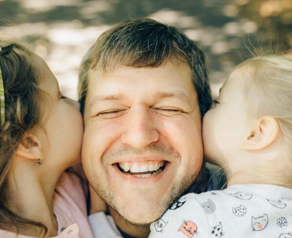 Photo by Nataliya Vaitkevich: https://www.pexels.com/photo/close-up-of-a-man-being-kissed-by-his-daughters-5290404/